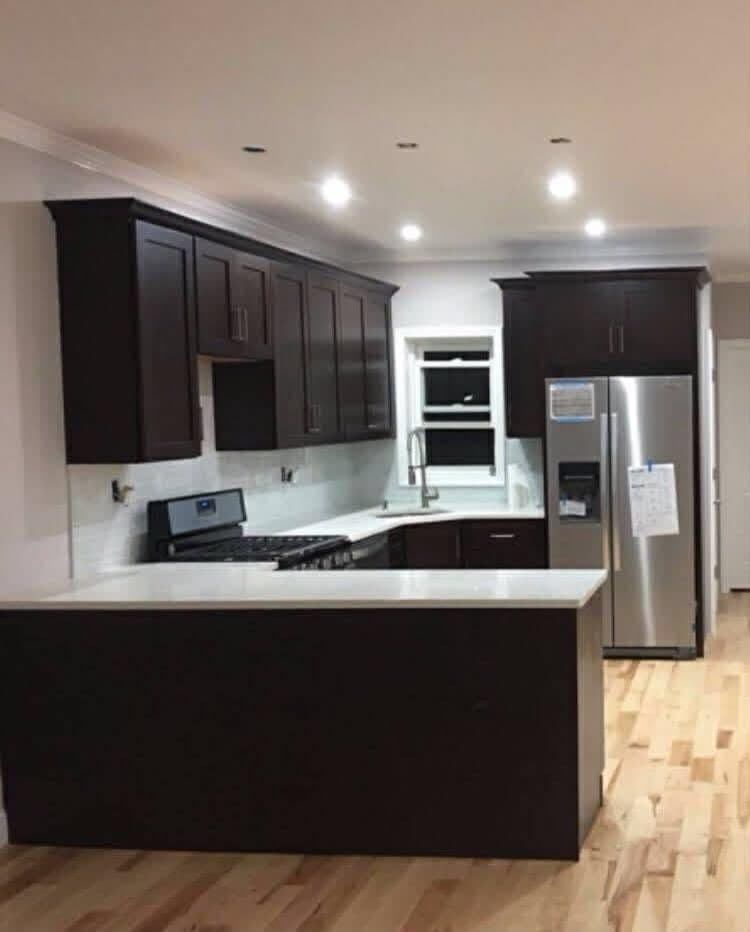 Completed kitchen with dark cabinetry, light counters and recessed lighting