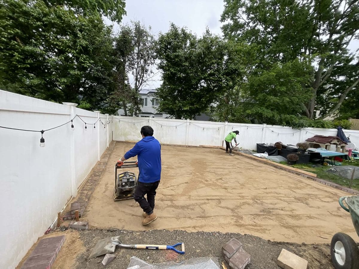 Crew compacting the graded base of a yard before paver installation