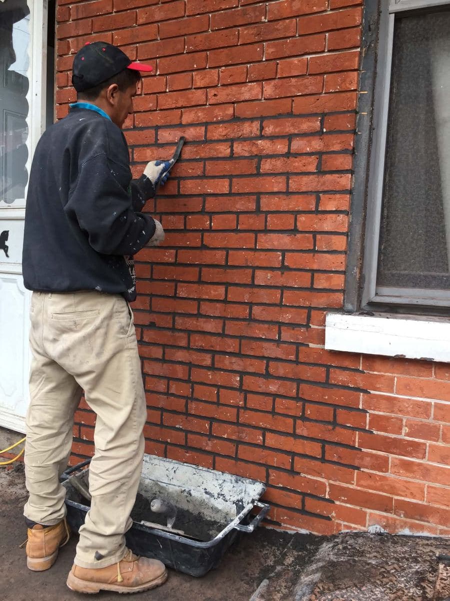 Mason reviewing and treating the face of a red brick wall
