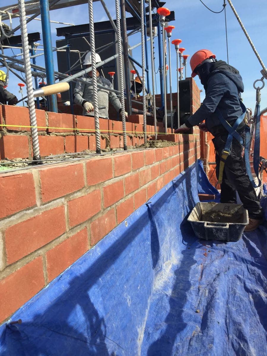 Worker with a mortar tray pointing a parapet wall beside scaffolding